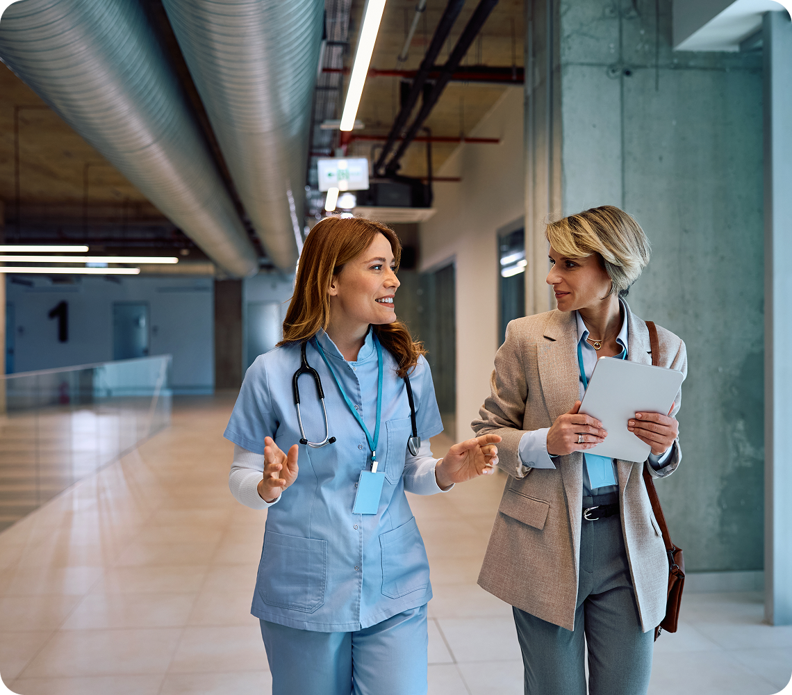Doctor and businesswoman walking, discussing in hallway.